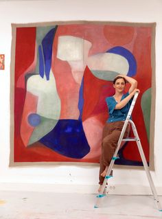 a woman sitting on a ladder in front of a painting