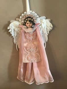 an angel doll hanging on the wall with pink satin and white lace around it's wings