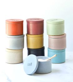 several different colors of ceramic containers with wooden spoons next to each other on a white surface