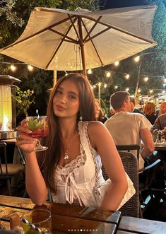 a woman sitting at a table with a drink in her hand and an umbrella over her head