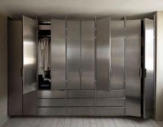 an empty room with stainless steel lockers and clothes hanging on the door, in front of a wooden floor