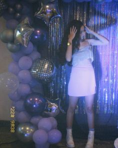 a woman standing in front of balloons with her hand on her head and hands behind her head