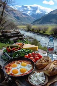 an assortment of food on a picnic table with mountains in the background