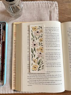 an open book sitting on top of a wooden table next to a jar of pens