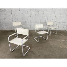 three white chairs sitting next to each other on concrete floored area with brick wall in background