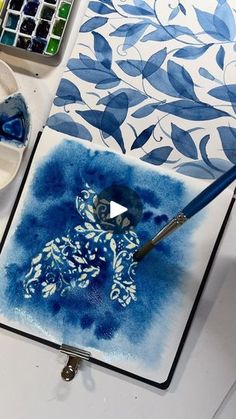 a blue and white painting on top of a table next to some paintbrushes