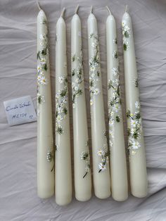 five candles with daisies painted on them sitting on a white cloth covered tablecloth