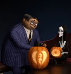 two people in halloween costumes sitting at a table with carved pumpkins