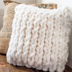 a white knitted pillow sitting on top of a wooden table