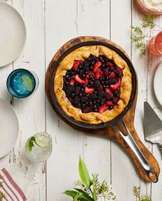 a pie with berries and strawberries in it sitting on a wooden board next to plates