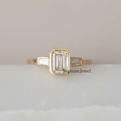 an emerald and baguette diamond engagement ring on a white surface with a light pink background