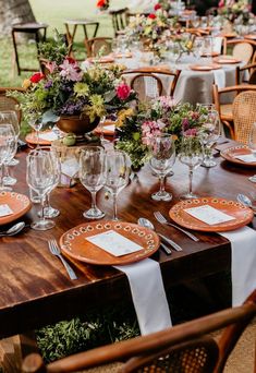 an outdoor table set with place settings and flowers in vases on the top, along with empty wine glasses