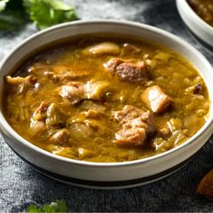 two bowls filled with meat and vegetable soup on top of a blue cloth covered table