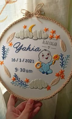 a hand holding up a white embroidered birth plaque with an image of a bear on it