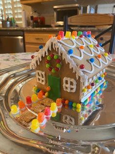 a gingerbread house decorated with candy and candies on a glass platter in a kitchen