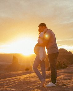 a man and woman standing in the desert at sunset