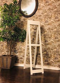 a white ladder leaning against a stone wall next to a potted plant and mirror