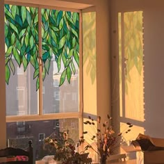 the sun shines through two windows with green leaves on them, in front of a dining room table and chairs