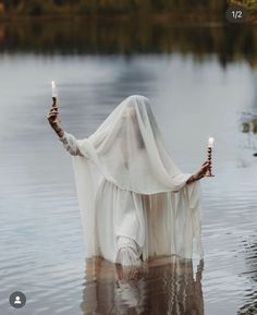 a woman with two candles in her hands standing in the water holding an open cloth over her head