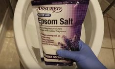 a person holding up a tube of epsom salt in front of a toilet bowl