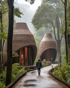 a man walking down a path in the woods with two stone huts on either side