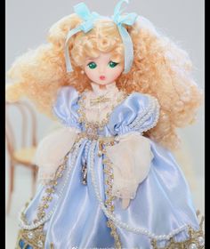 a doll with blonde hair wearing a blue dress and pearls on it's head