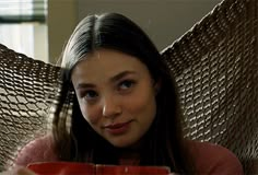 a woman sitting in a hammock holding a red cup and looking at the camera