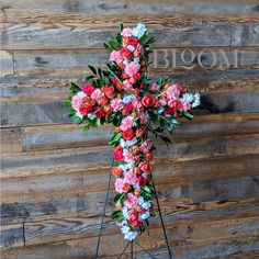 a cross made out of flowers sitting on top of a wooden floor next to a wall