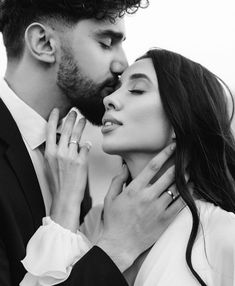 a man kissing a woman's face while she is wearing a white shirt and black suit