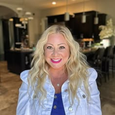 a woman with blonde hair standing in front of a kitchen and dining room area, smiling at the camera