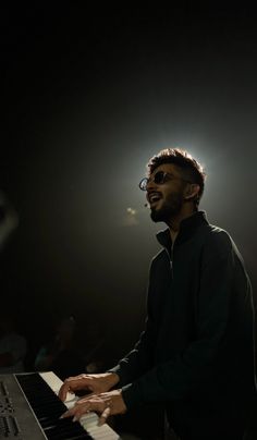 a man with glasses playing the piano in front of a microphone and spotlights behind him