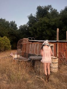 a woman in a pink dress standing next to an old birdcage and looking into the distance