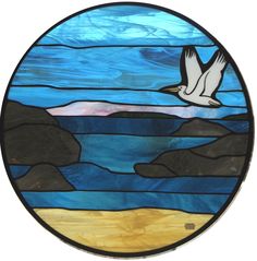 a round stained glass window with a seagull flying over the ocean and mountains