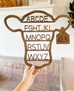 a person holding up a wooden cut out of a cow's head with the letters below it