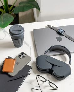 an apple laptop, headphones, and other items on a white table with a cup of coffee