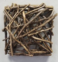 a square sculpture made out of branches on a white wall with no one in it