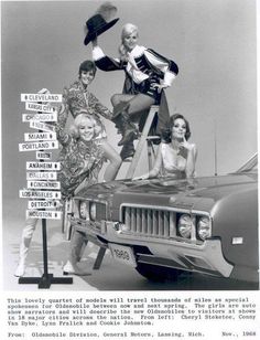 four women standing on top of a jeep with street signs in front of them, all pointing to different directions