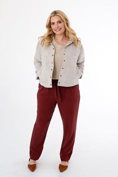 a woman standing in front of a white background wearing red pants and a button up shirt