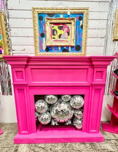 a pink fireplace with lots of disco balls on it's mantle in front of a painting