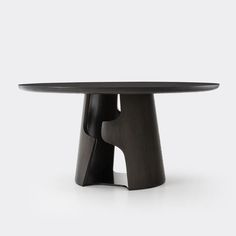 a black table with an oval top and curved legs, on a white surface in front of a gray background