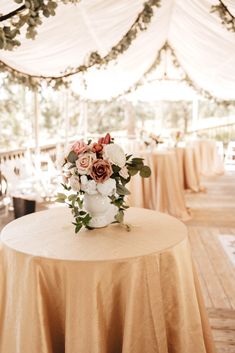 a table topped with a vase filled with flowers next to tables covered in white linens