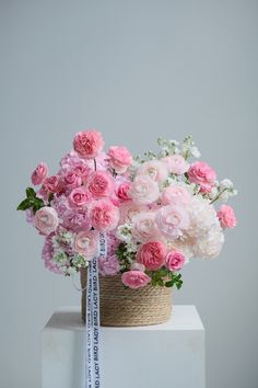 pink and white flowers in a basket with a ribbon tied around the end on a pedestal