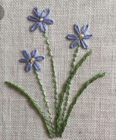 three blue flowers with green stems on a white cloth