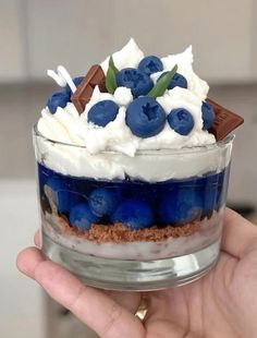 a person holding up a dessert in their hand with blueberries and whipped cream on top