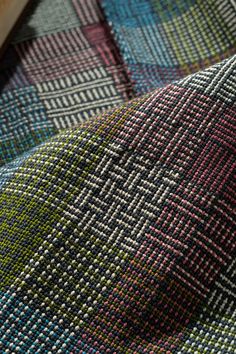 a close up view of a multicolored checkered fabric with an unfinished piece of wood in the background