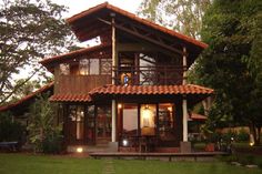 a small house with an open porch in the middle of some trees and grass, at dusk