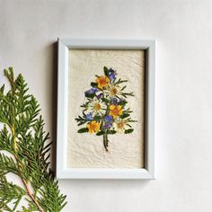 a white frame with some yellow and blue flowers on it next to a pine branch