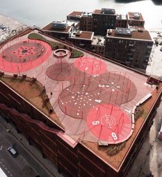 an aerial view of a large building with red paint on it's roof and some buildings in the background