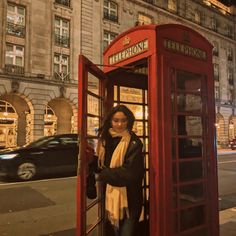 a woman standing in a red phone booth on the side of a street at night