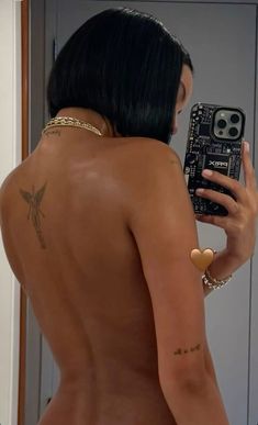 a woman taking a selfie in the mirror with her cell phone and tattoos on her back